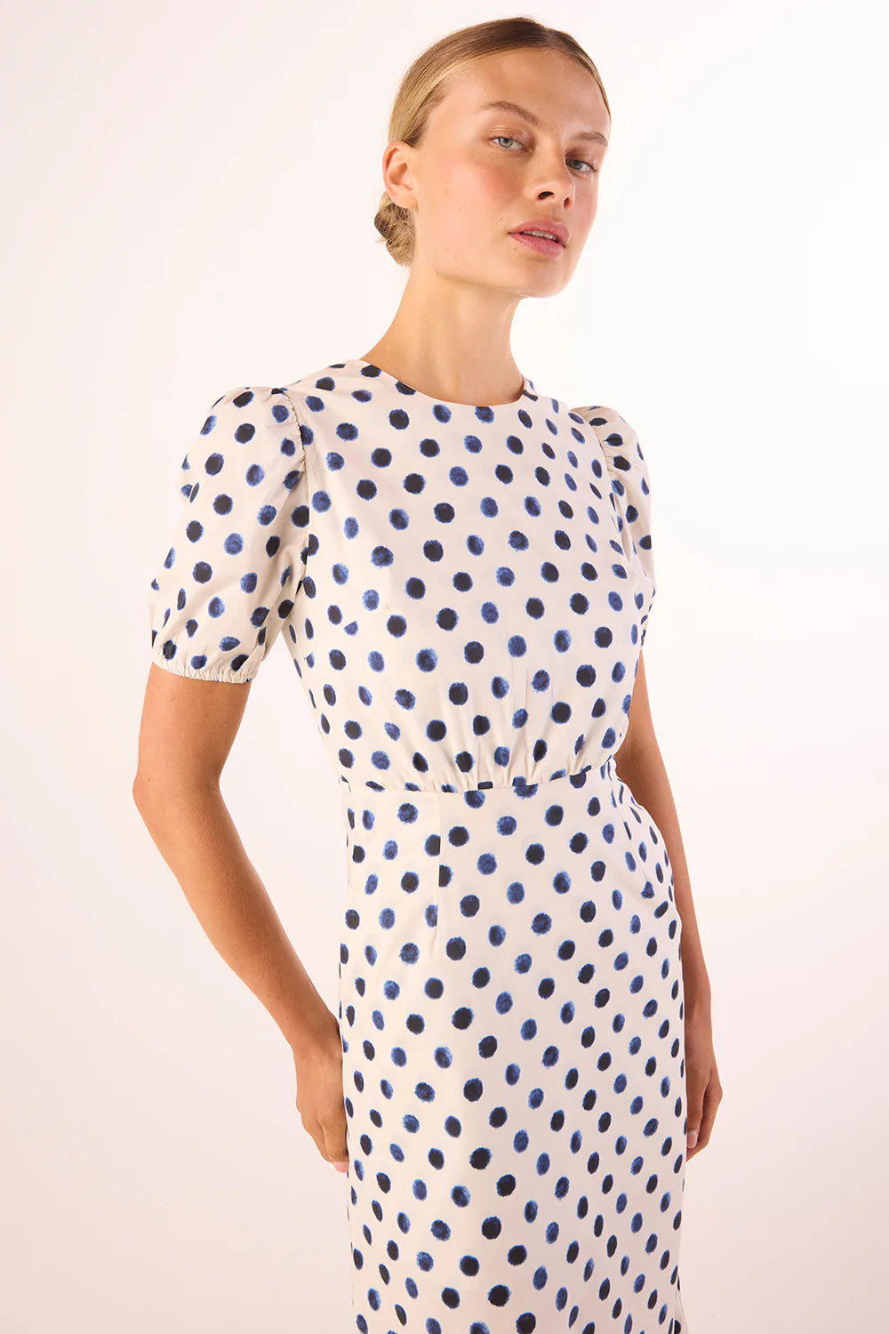 Woman wearing a white dress with blue polka dots against a plain background