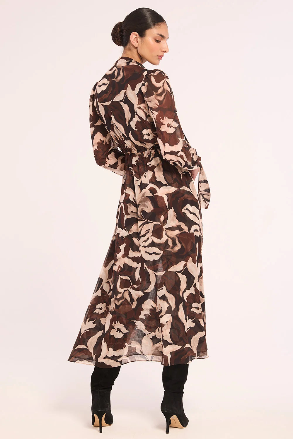 A woman modeling a long-sleeved midi wrap dress with a brown and beige floral pattern, shown from a side-back angle against a plain white studio background.