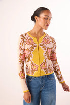 Woman wearing a floral cardigan over a yellow shirt with blue jeans on a white background