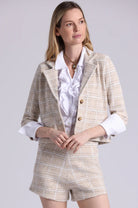 Woman wearing a beige tweed suit with a white shirt on a light gray background