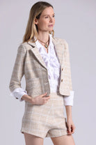Woman wearing a beige checkered blazer and shorts set on a light gray background