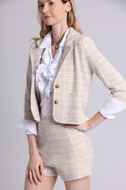 Woman wearing a beige blazer and shorts set with a white shirt on a plain background