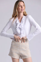 Woman wearing a white blouse with ruffled details and beige shorts on a light gray background