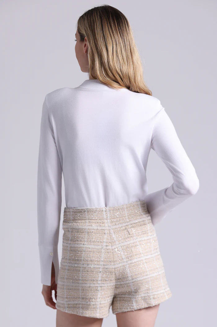 Woman wearing a white long-sleeve top and beige shorts on a light gray background