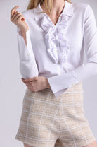 White blouse with ruffled details worn by a person on a plain background