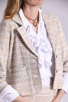 Person wearing a beige tweed jacket over a white shirt with a necklace.
