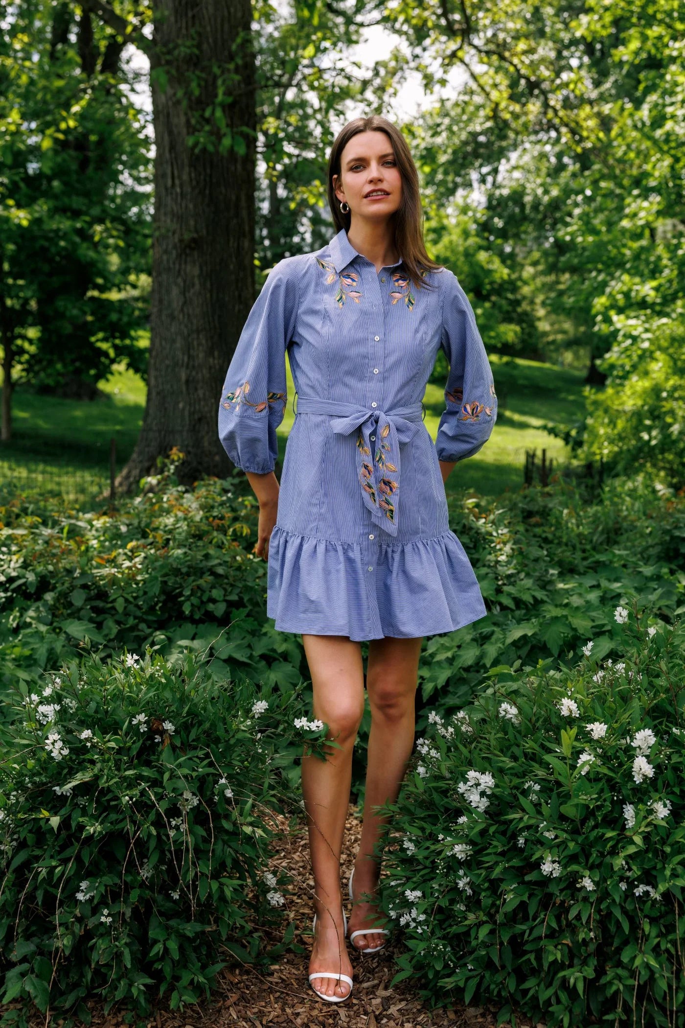 Woman in a blue dress standing in a garden with greenery and flowers.
