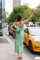 Woman in a green dress waving at a yellow taxi in an urban setting