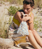 Woman sitting on a log by a body of water, holding a sequined bag.