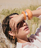 Woman with a large orange bracelet on her wrist, standing in a natural setting.