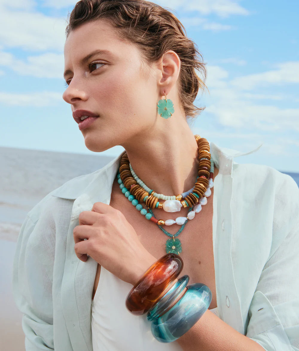 Woman wearing a stack of necklaces and earrings with a beach background