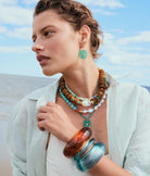 Woman wearing a stack of necklaces and earrings with a beach background