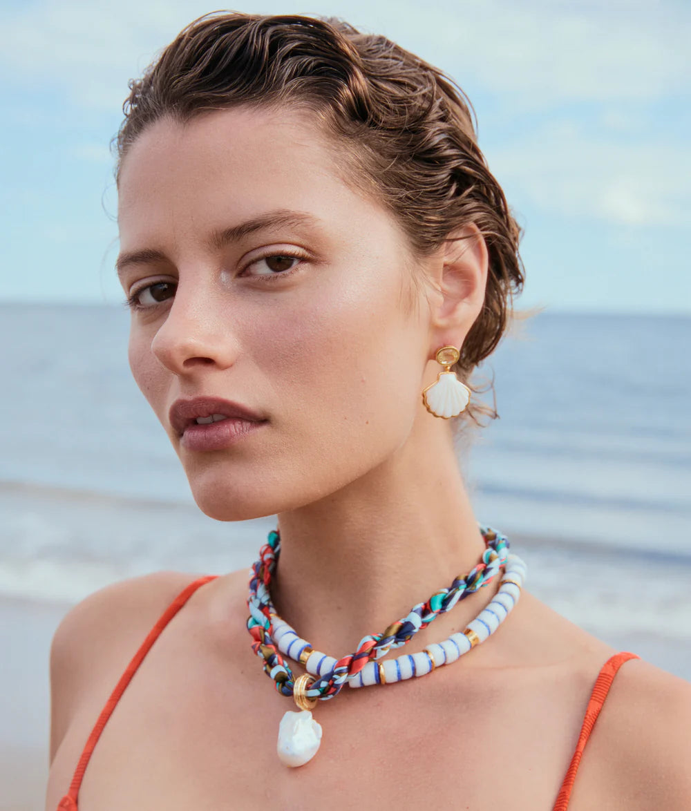 Woman wearing a colorful beaded necklace and earrings with a beach background
