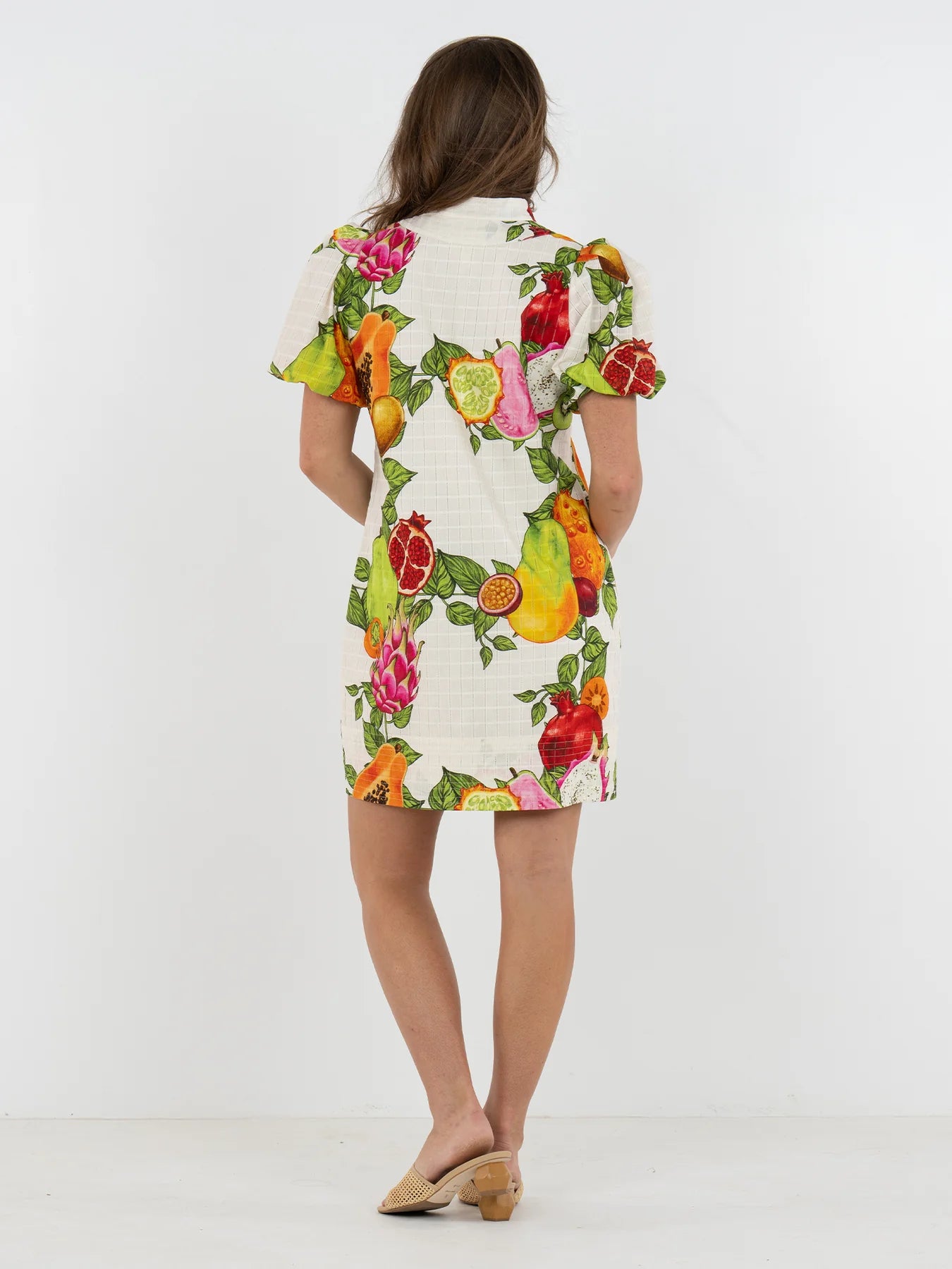 Woman wearing a colorful fruit print dress on a white background