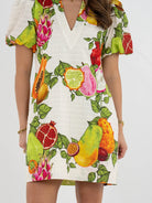 White dress with colorful fruit print worn by a person on a white background