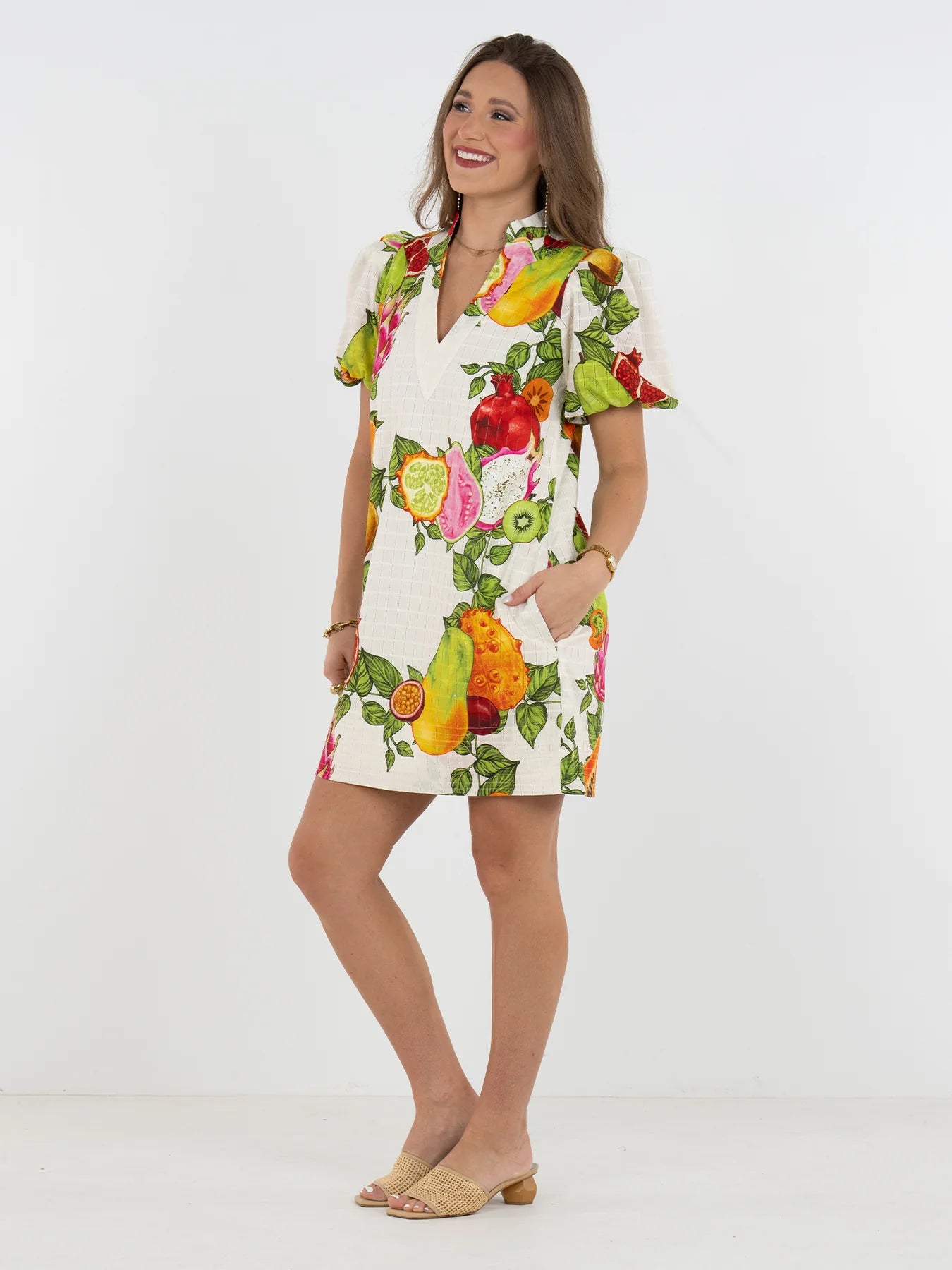 Woman wearing a colorful fruit-print dress on a white background