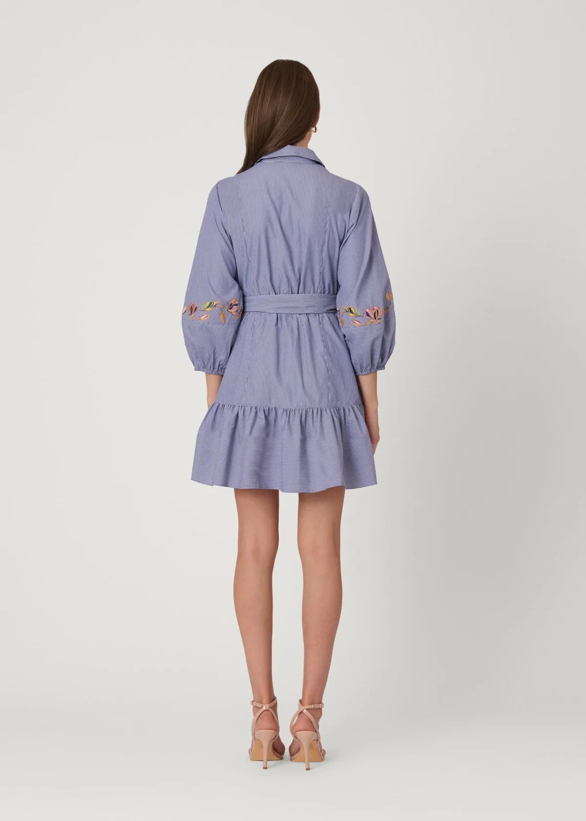 Woman wearing a light blue dress with floral embroidery on a white background
