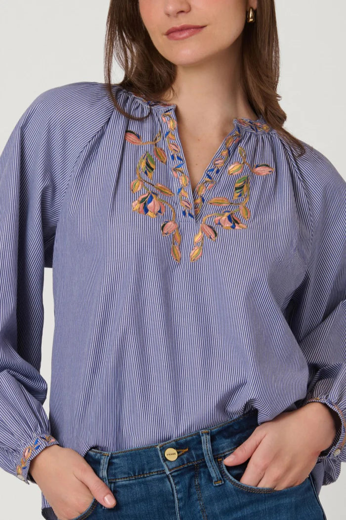 Woman wearing a blue striped blouse with floral embroidery on a white background