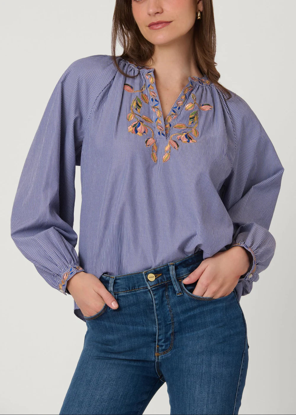 Woman wearing a blue blouse with floral embroidery and blue jeans on a white background