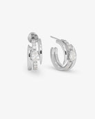 A pair of silver-toned huggie hoop earrings with clear marquise-cut and round stones, shown from side and front angles on a light gray background.