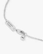 Silver necklace with engraved tag and heart-shaped charm on a white background
