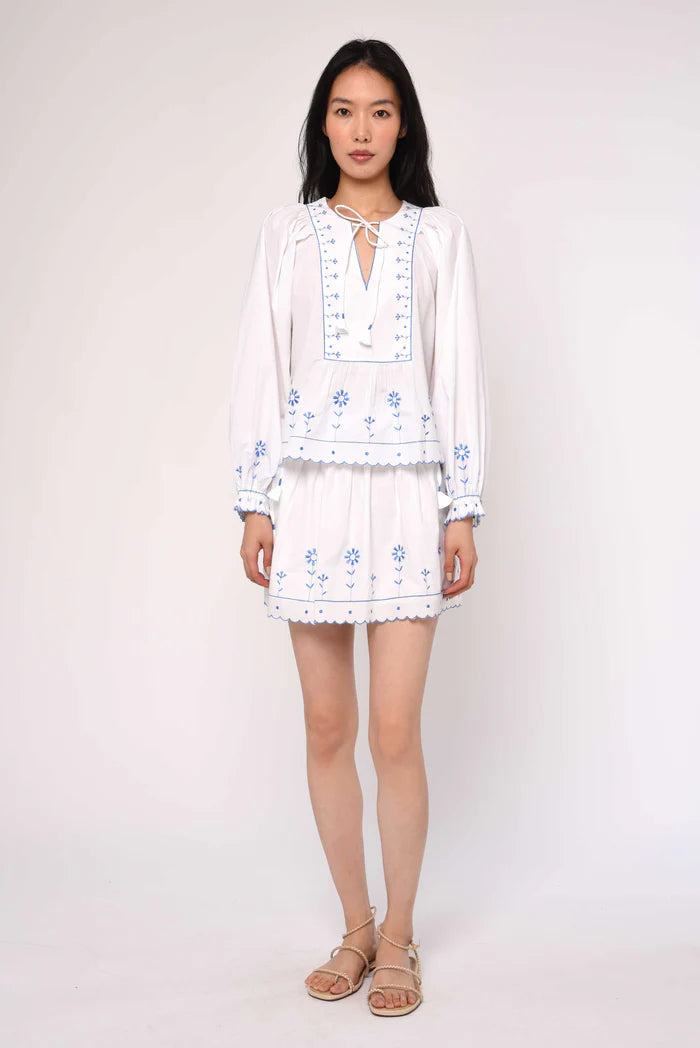 Woman wearing a white embroidered dress on a plain background