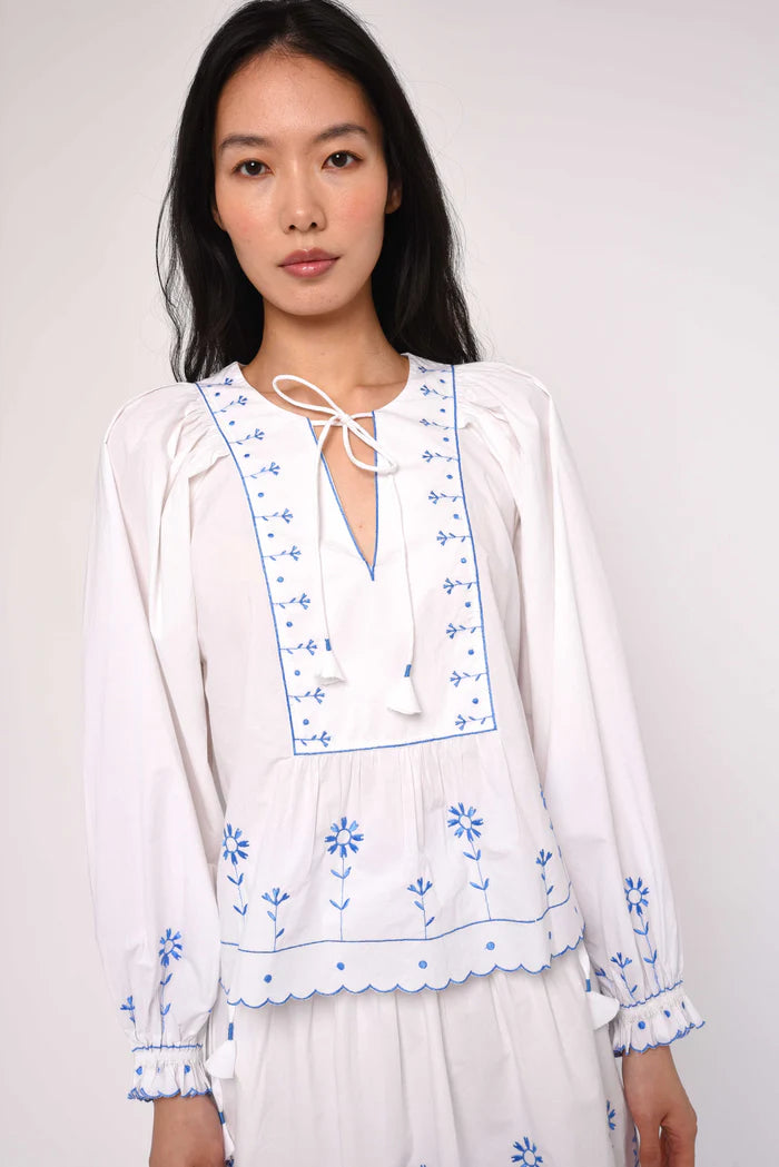 Woman wearing a white blouse with blue embroidery on a plain background