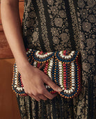 Hand holding a colorful beaded clutch against a patterned background