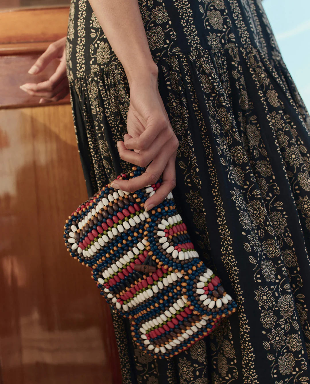 Person holding a beaded clutch with a patterned dress in the background