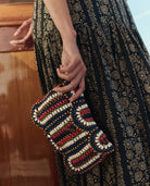 Person holding a beaded clutch with a patterned dress in the background