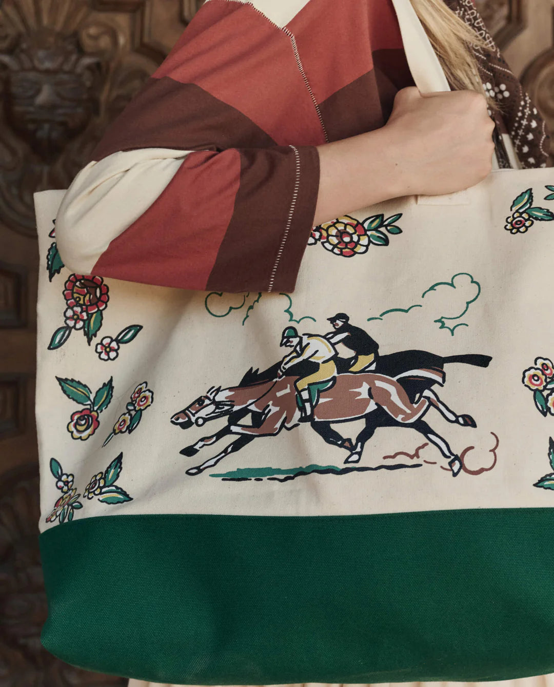 Tote bag with horse and floral design held by a person wearing a patchwork jacket.