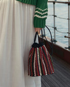 Person holding a multicolored woven bag on a boat deck.