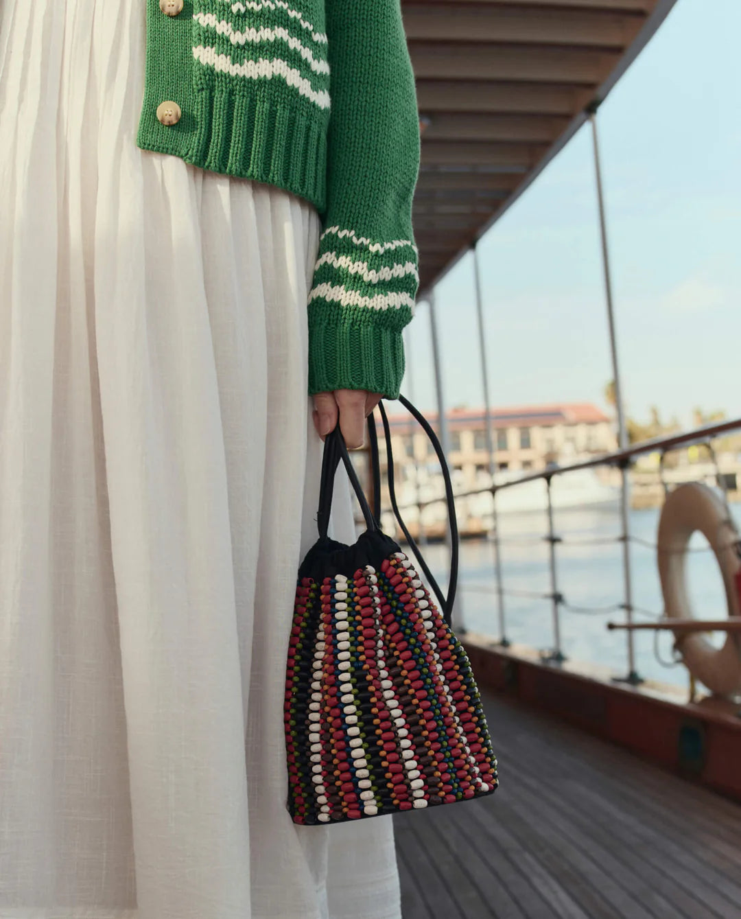 Person holding a multicolored woven bag on a boat deck.