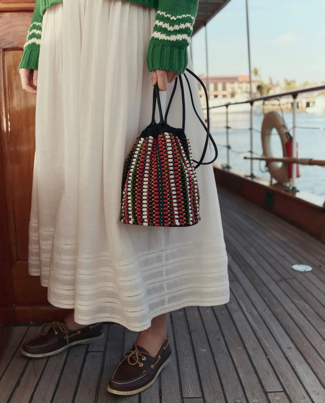 Person holding a multicolored woven bag on a boat deck.