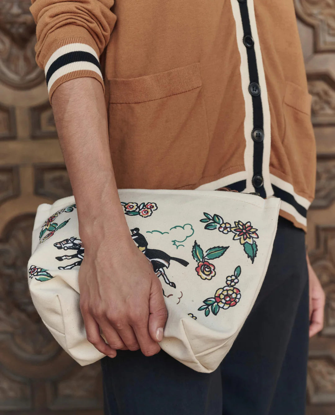 Person holding a white bag with floral and horse designs against a textured wall.