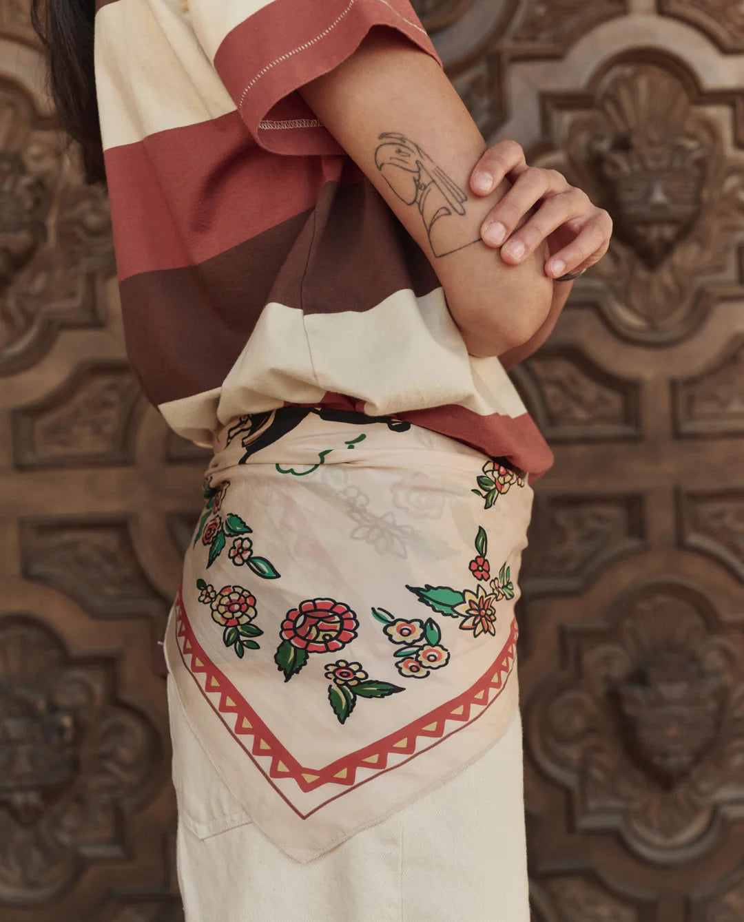 Person wearing a colorful outfit with floral embroidery against a decorative wooden background