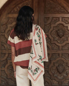 Person wearing a striped shirt and embroidered scarf in front of a wooden door with intricate carvings.