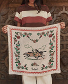 Person holding a decorative towel with horse and floral design against a wooden background