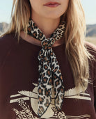 Person wearing a leopard print scarf with a brown top featuring white patterns.