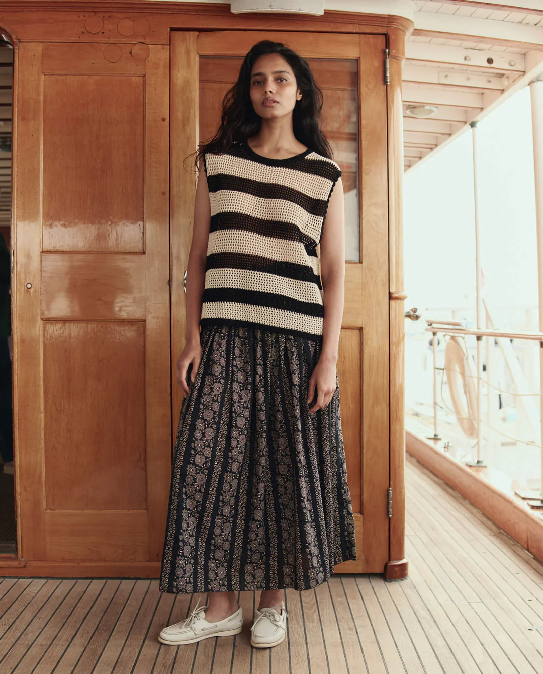 Woman wearing a black and white striped sleeveless top and a long black lace skirt on a wooden deck.