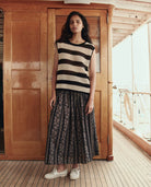 Woman wearing a black and white striped sleeveless top and a long black lace skirt on a wooden deck.