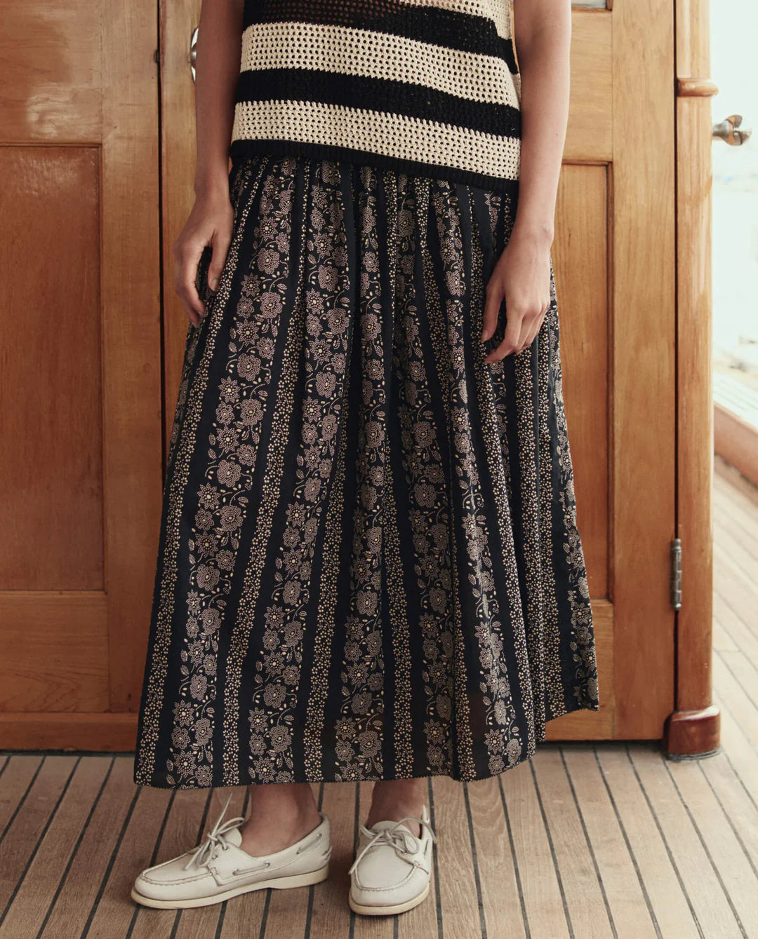 Person wearing a black and white striped top and patterned skirt standing in front of a wooden door.