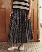 Person wearing a black and white striped top and patterned skirt standing in front of a wooden door.