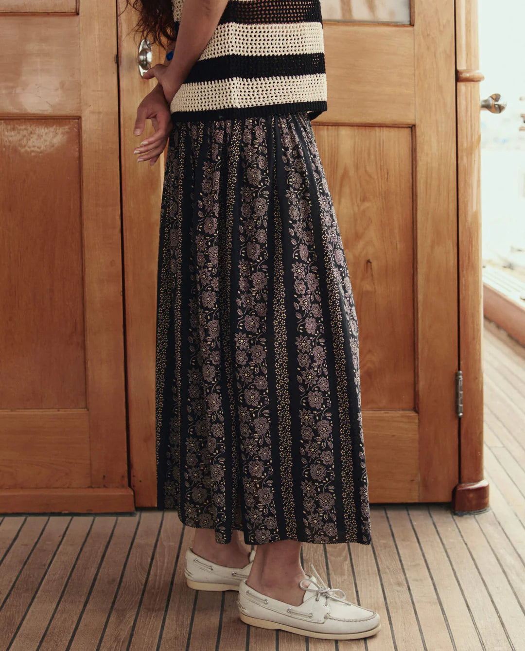 Person wearing a black and white striped top and a long black lace skirt on a wooden deck.