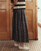 Person wearing a black and white striped top and a long black lace skirt on a wooden deck.
