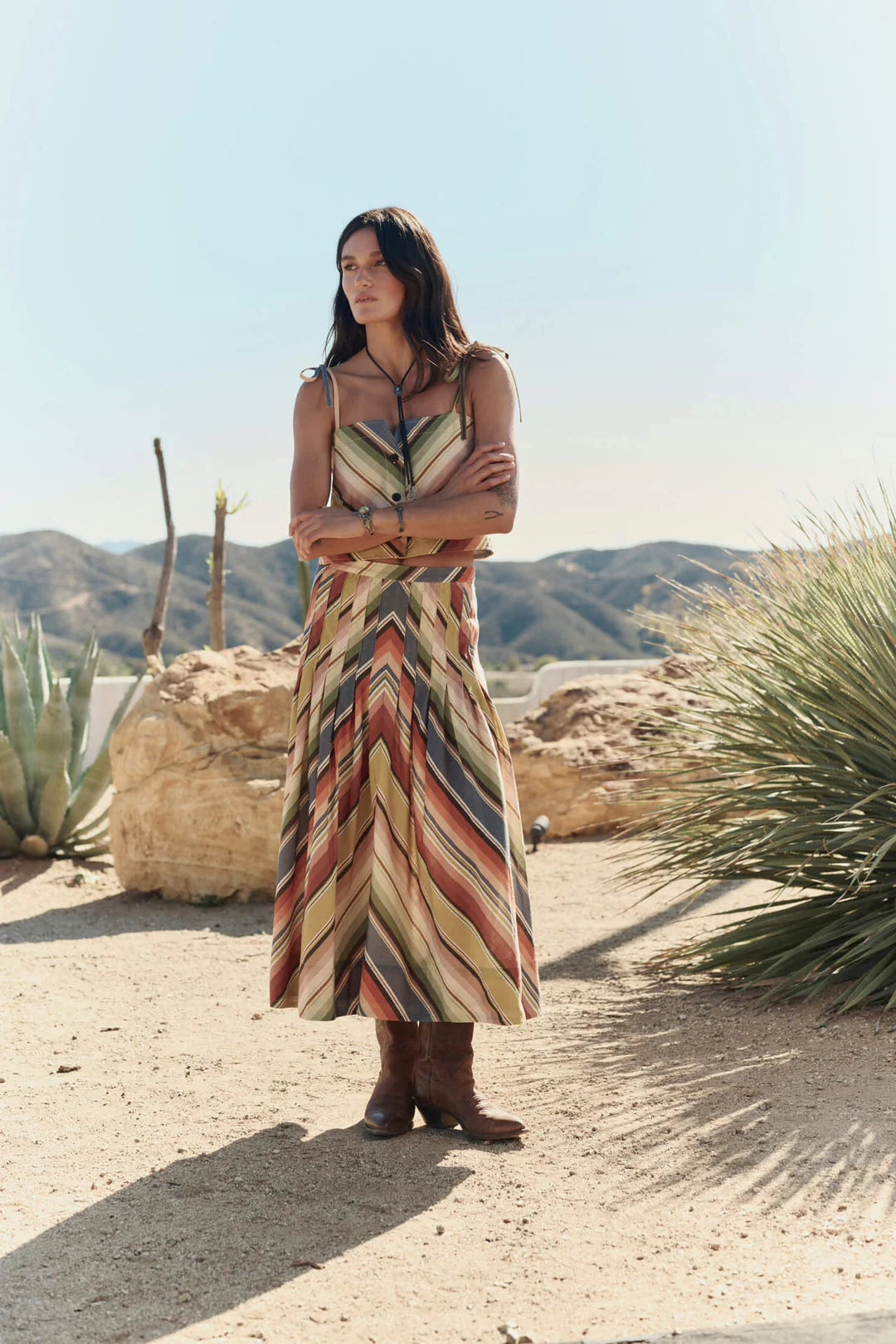 Woman in a colorful dress standing in a desert landscape with mountains in the background