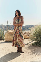 Woman in a colorful dress standing in a desert landscape with mountains in the background