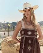 Woman wearing a brown dress with white patterns and a straw hat in a desert setting.