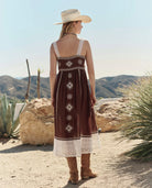 Woman in a brown dress with white lace trim standing in a desert landscape.