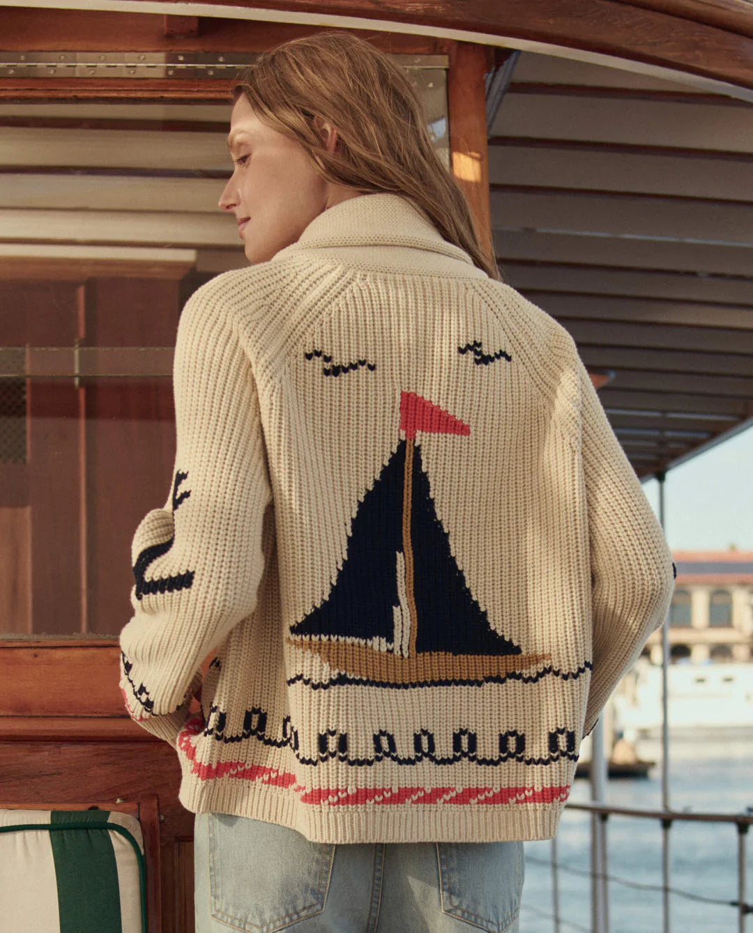 Person wearing a cream-colored sweater with sailboat design on a boat deck.